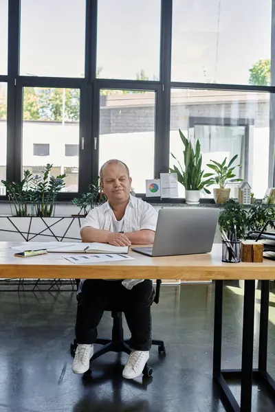 A man with inclusivity sits at a desk in an office setting, working on a laptop computer. — Stock Photo
