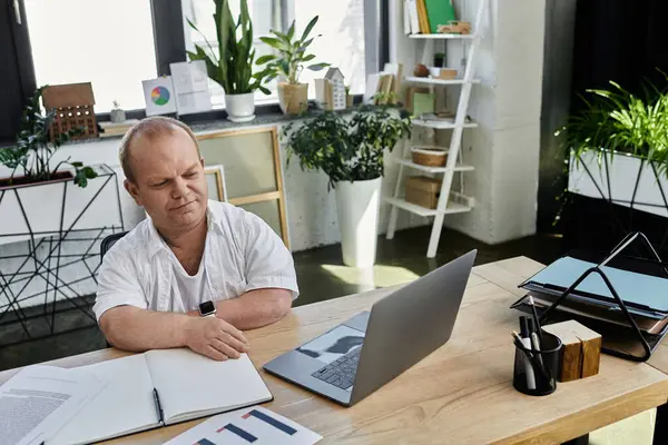Un homme inclusif travaille à son bureau dans un bureau moderne, concentré sur son ordinateur portable et ses documents. — Photo de stock