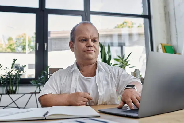 Un homme avec inclusivité est assis à un bureau dans un bureau moderne, concentré sur son ordinateur portable. — Photo de stock