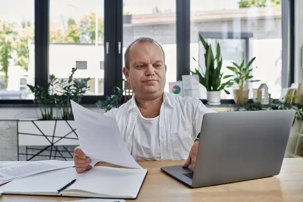 Un homme inclusif travaille avec diligence sur son ordinateur portable et ses papiers dans un espace de bureau bien éclairé. — Photo de stock