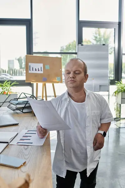 Un hombre con inclusividad en una camisa blanca está junto a un escritorio en una oficina, revisando documentos. — Stock Photo