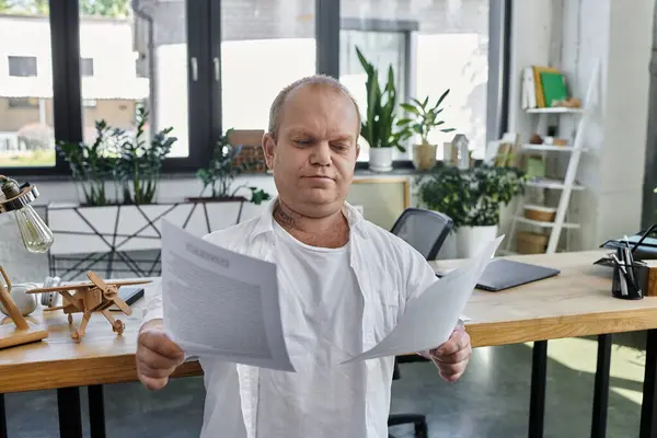 Um homem com inclusividade em uma camisa branca senta-se em uma mesa em um escritório, revisando cuidadosamente documentos. — Fotografia de Stock