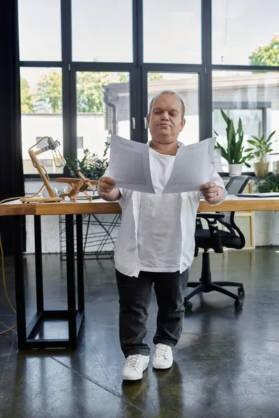 Ein Mann mit Inklusivität steht in einem modernen Büro, überprüft Dokumente und bewahrt dabei einen konzentrierten Ausdruck. — Stockfoto