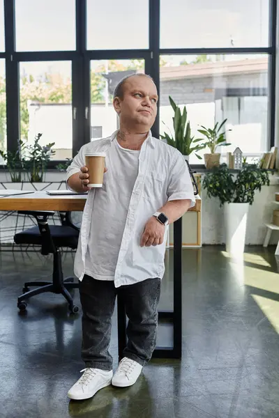 A man with inclusivity stands in an office setting, holding a cup of coffee. — Stock Photo