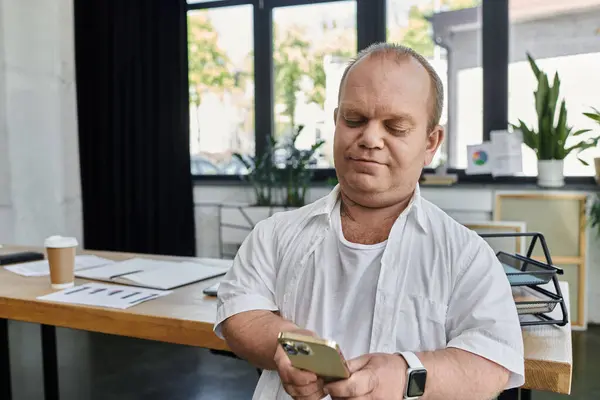 A man with inclusivity sits at a desk in an office, intently looking at his phone. — Stock Photo