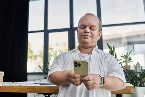 A man with inclusivity sits in a modern office setting, checking his phone. — Stock Photo