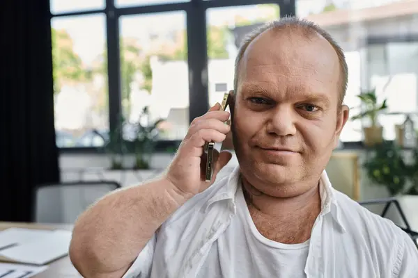 Человек с инклюзивностью сидит за своим столом, делая телефонный звонок, работая в своем домашнем офисе. — стоковое фото