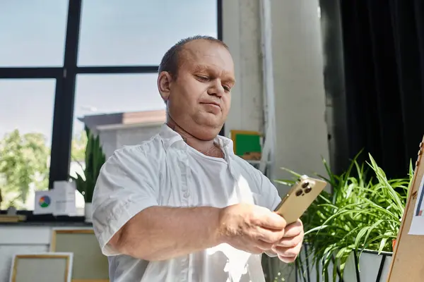 Um homem com inclusividade usando uma camisa branca usa seu telefone em um escritório iluminado pelo sol. — Fotografia de Stock