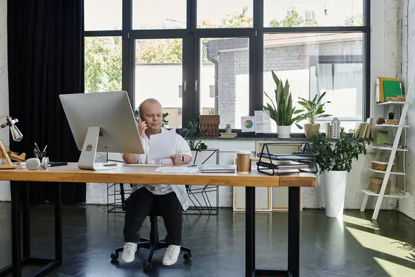 Un uomo con inclusività siede alla sua scrivania in un ufficio, lavorando al suo computer. — Foto stock