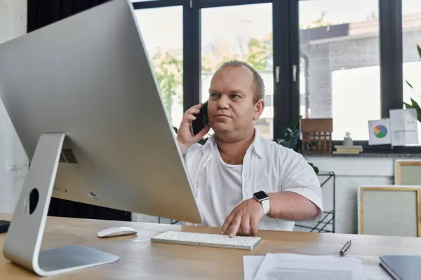 A man with inclusivity in a modern office works on his computer while talking on the phone. — Stock Photo