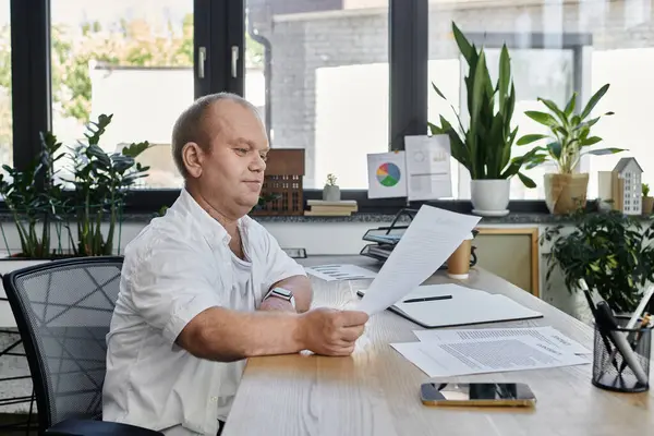 A man with inclusivity sits at his desk in a well-lit office, reviewing documents. — Stock Photo