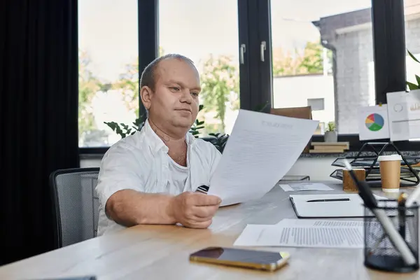 Un uomo con inclusività si siede a una scrivania in un ufficio, rivedendo documenti. — Foto stock