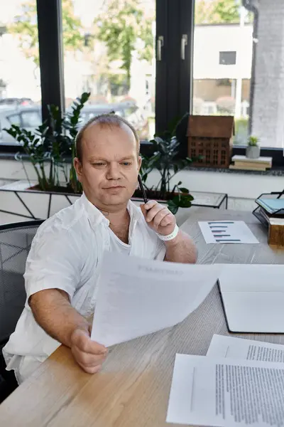 A man with inclusivity sits at a desk, reviewing documents in a well-lit office. — Stock Photo