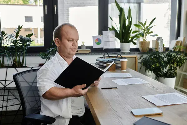 Чоловік з інклюзивністю у білій сорочці сидить в сучасному офісі, переглядаючи документи за своїм столом. — стокове фото