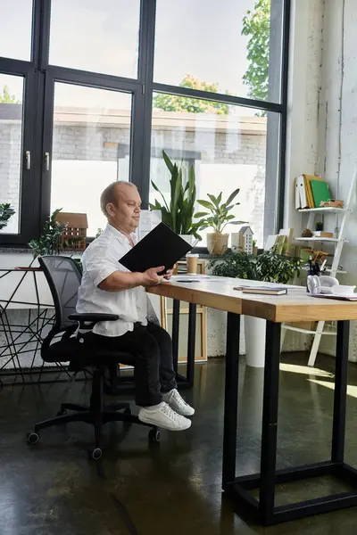 A man with inclusivity sits at a desk in a bright office, working on a document. — Stock Photo