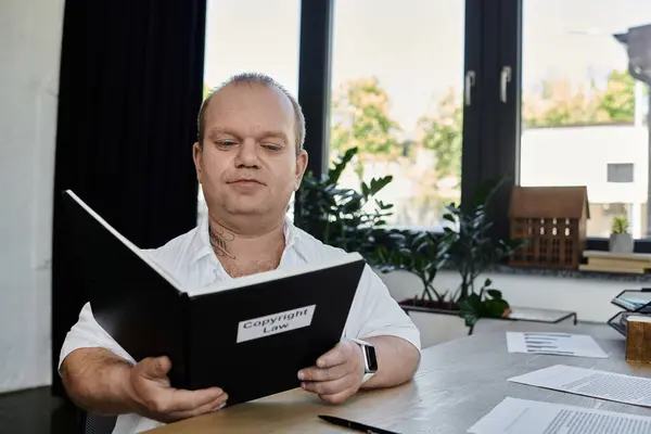 Um homem com inclusividade senta-se em um escritório, lendo um livro intitulado Direito Autoral. — Fotografia de Stock