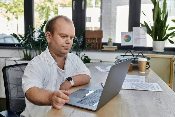 A man with inclusivity sits at his desk in an office, working on his laptop. — Stock Photo