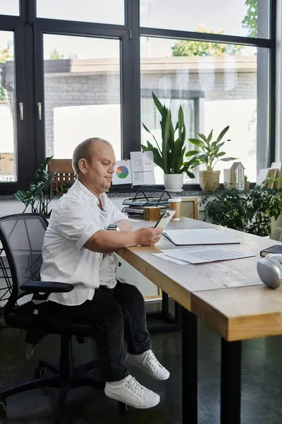 A man with inclusivity sits at his desk in an office, working on a task. — Stock Photo