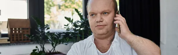 Мужчина с инклюзивностью в белой рубашке отвечает на телефонный звонок, сидя у окна в своем кабинете. — стоковое фото