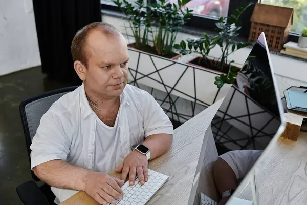 A man with inclusivity sits at a desk in a modern office, working on a computer. — Stock Photo