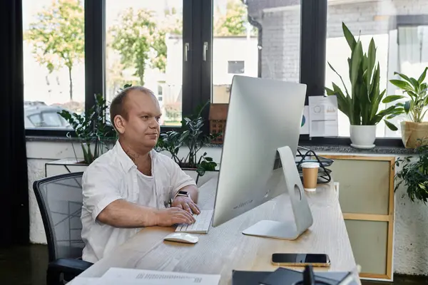 A man with inclusivity sits at a desk in an office, working on a computer. — Stock Photo