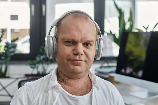 Un hombre con inclusividad usando auriculares trabaja en su escritorio en una oficina moderna. - foto de stock