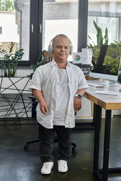 Un homme inclusif travaille à un bureau, portant des écouteurs, incarnant l'inclusivité et la productivité.. — Photo de stock