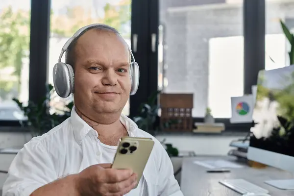 A man with inclusivity wearing headphones sits at his desk in an office setting. — Stock Photo