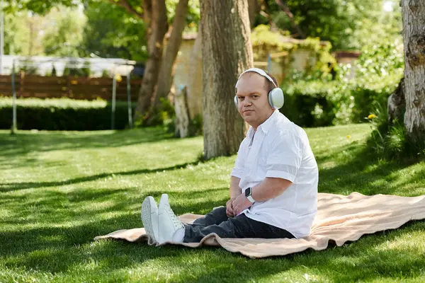 A man with inclusivity relaxes on a blanket in a park, listening to music with headphones. — Stock Photo