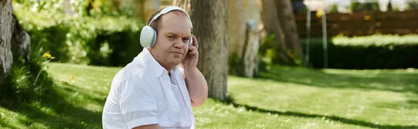 A man with inclusivity in headphones walks through a grassy park, enjoying the sunny afternoon. — Stock Photo