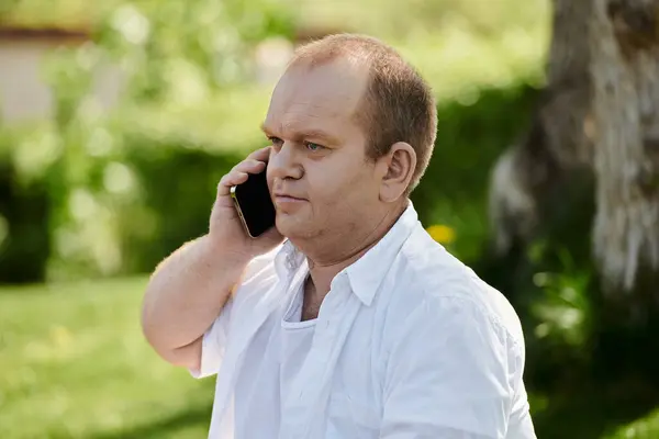 Человек с включённостью в белой рубашке разговаривает по телефону во время прогулки по парку. — стоковое фото