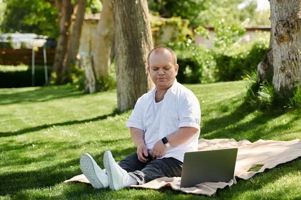 Un hombre con inclusividad se sienta en una manta en un parque, usando una computadora portátil. — Stock Photo