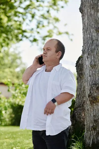 A man with inclusivity stands by a tree, talking on his phone. — Stock Photo