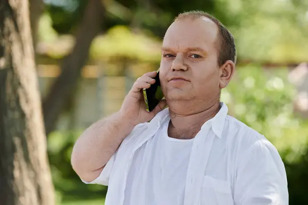 Un hombre con inclusividad camina por un parque, hablando por teléfono en un día soleado. — Stock Photo