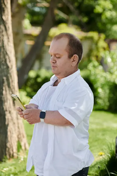 A man with inclusivity in a white shirt uses his phone while walking through a park on a sunny day. — Stock Photo