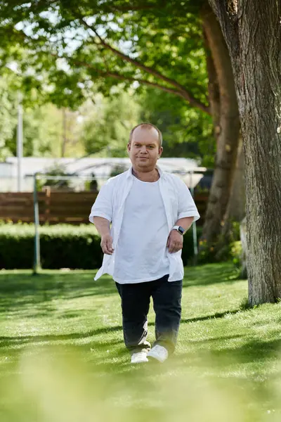 A man with inclusivity walks on a green lawn, surrounded by lush trees on a sunny day. — Stock Photo