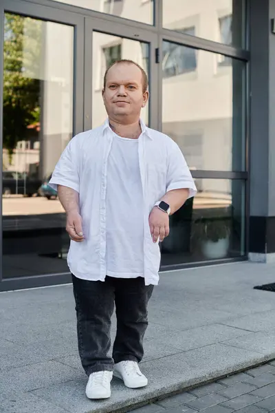 A man with inclusivity in a white shirt walks on a sidewalk outside a building with large glass doors. — Stock Photo