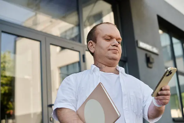 Чоловік з інклюзивністю виходить за межі сучасної офісної будівлі, використовуючи свій смартфон. — стокове фото