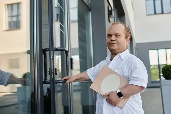 A man with inclusivity exits a building, holding a folder, while wearing a white shirt. — Stock Photo