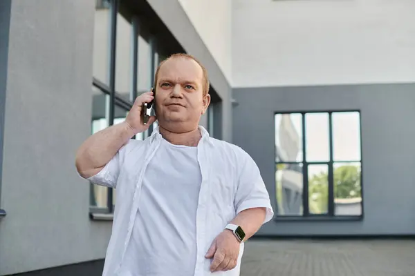 A man with inclusivity walks confidently towards a window, talking on his phone. — Stock Photo