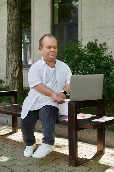 Un uomo con inclusività si siede su una panchina del parco fuori, lavorando sul suo computer portatile. — Foto stock