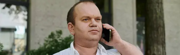 Un hombre con inclusividad en una camisa blanca habla por teléfono fuera de un edificio. - foto de stock