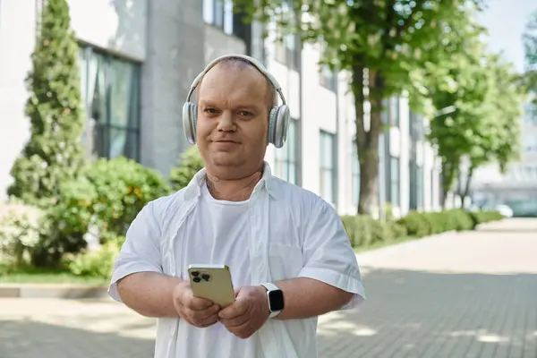 A man with inclusivity walks through a city, enjoying his music and the urban scenery. — Stock Photo