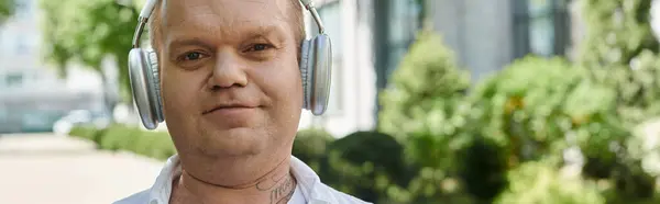 A man with inclusivity walks in a city setting, lost in his own world while listening to music through headphones. — Stock Photo
