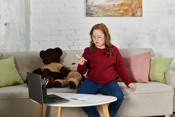 Little girl with Down syndrome on couch, holding pen. — Stock Photo