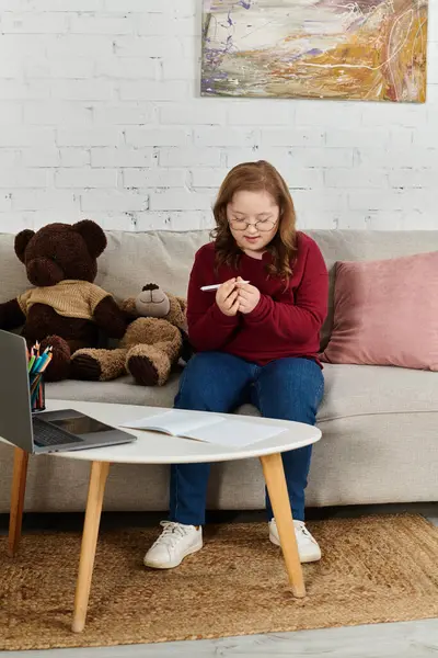 A little girl with Down syndrome sits on a couch and focuses on a pen in her hand. — Stock Photo