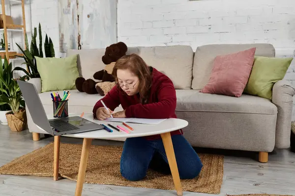 A little girl with Down syndrome draws at a small table in her living room. — Stock Photo