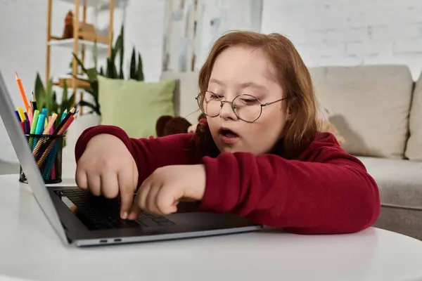 A little girl with Down syndrome is focused on her laptop while sitting at a table. — Stock Photo