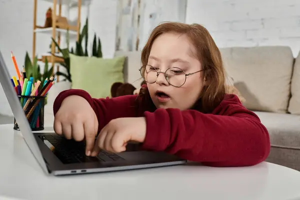 Una niña pequeña con síndrome de Down se centra en su computadora portátil mientras está sentada en una mesa. — Stock Photo