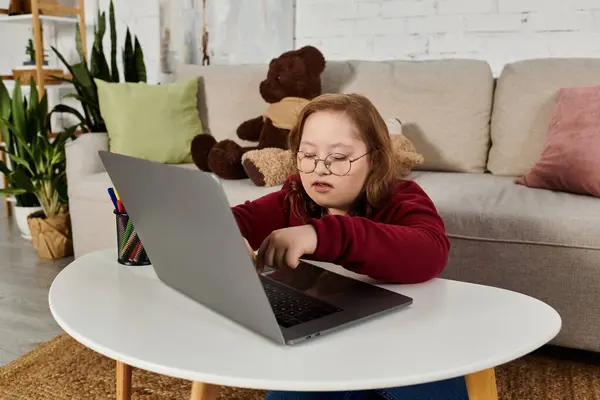 A little girl with Down syndrome uses a laptop in her living room. — Stock Photo